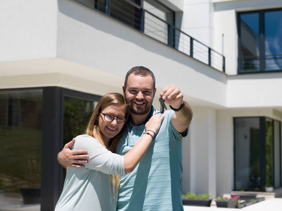 Happy young couple hugging in front of their new home they purchased with the first homebuyers loan.
